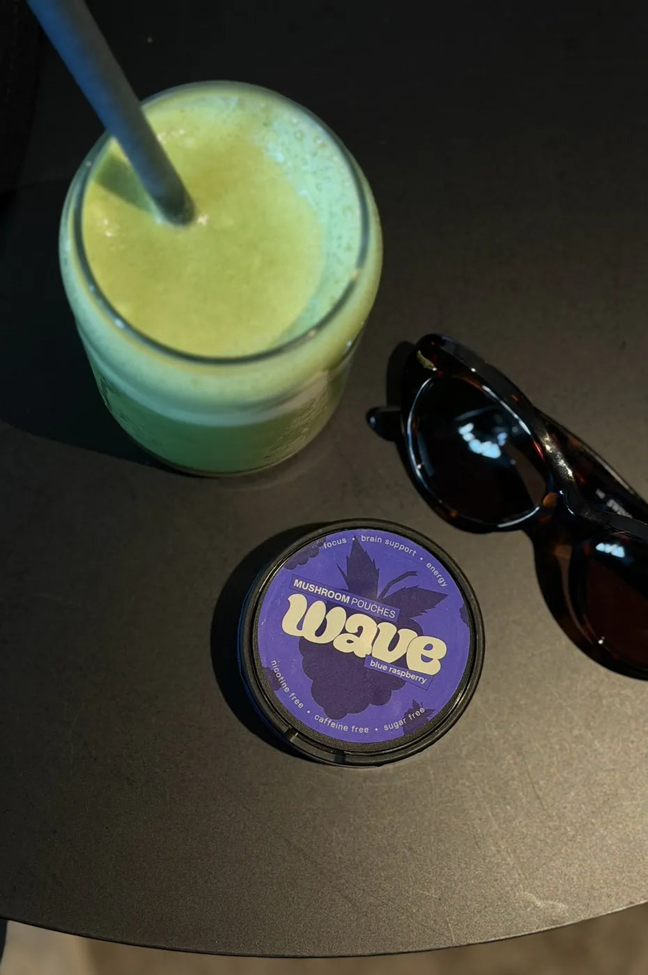 Puk WAVE na tmavom stole vedľa zeleného smoothie a slnečných okuliarov
